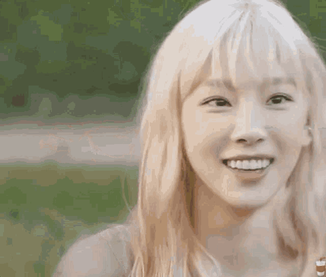 a close up of a woman with blonde hair smiling in a park .
