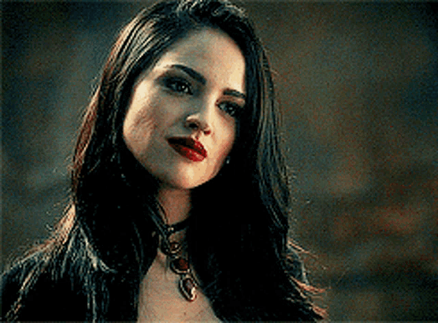a woman with long dark hair and red lips is wearing a choker necklace