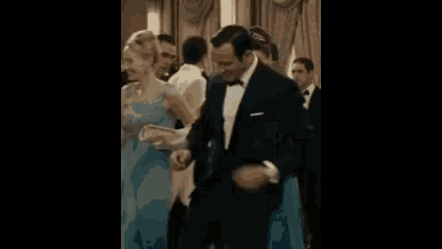 a man in a tuxedo is dancing with a woman in a blue dress at a formal event .