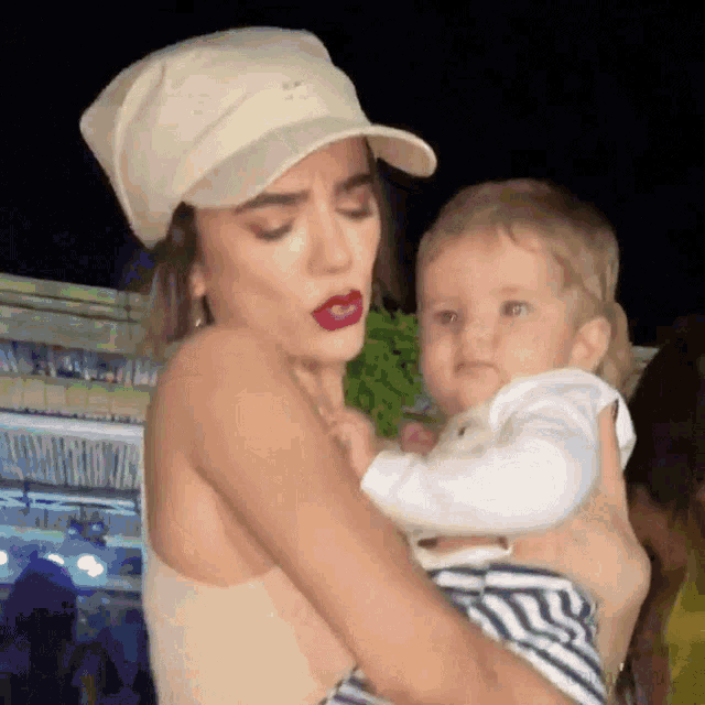 a woman wearing a hat holds a baby in her arms