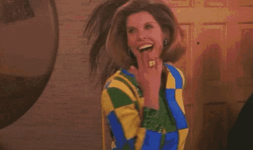 a woman wearing a colorful jacket is standing in front of a door and eating a candy bar .