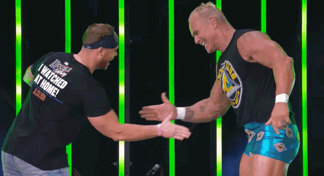 a man wearing a shirt that says ' i watched it at home ' on it shakes hands with another man