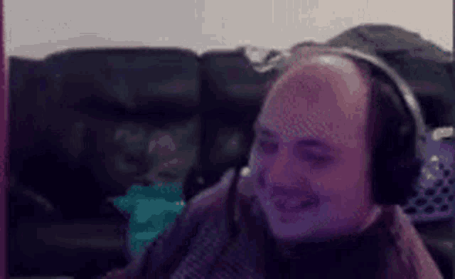 a bald man wearing headphones is smiling in front of a computer screen .