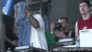 a man with a towel on his head is singing into a microphone while another man takes a picture