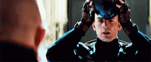 captain america is putting on his helmet in front of a bald man in a mirror .