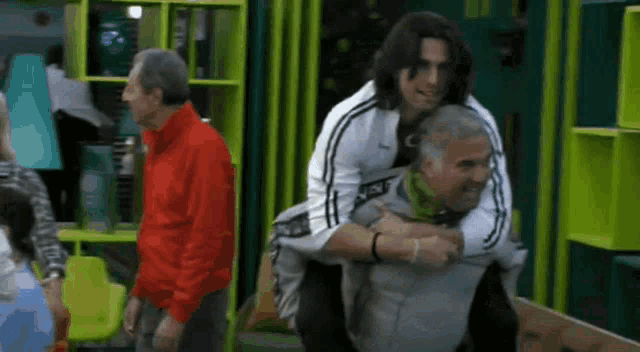 a man in a red jacket is carrying another man on his back ..