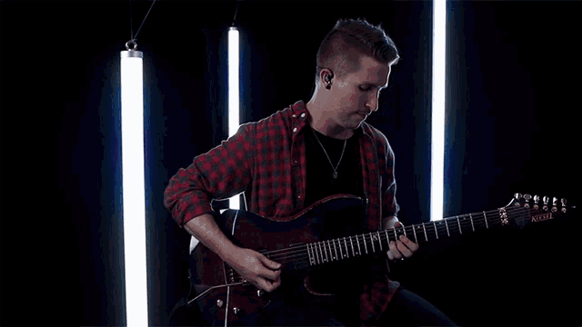 a man in a red plaid shirt is playing a guitar