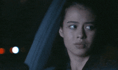 a woman is sitting in the driver 's seat of a car at night looking out the window .