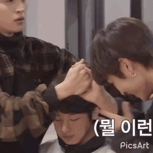 a man is cutting another man 's hair in a salon while another man looks on .