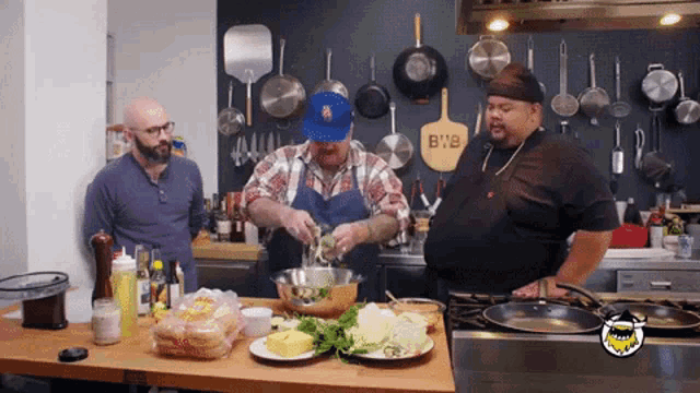three men are preparing food in a kitchen with a pizza paddle that says b'n'b on it