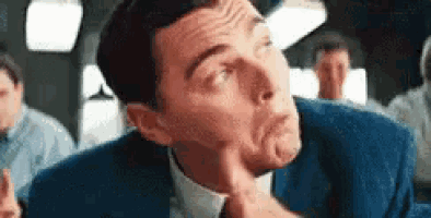 a man in a suit and tie is making a funny face while holding his hand to his chin .