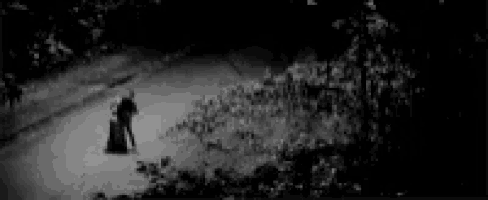a black and white photo of a person standing on a sidewalk at night .