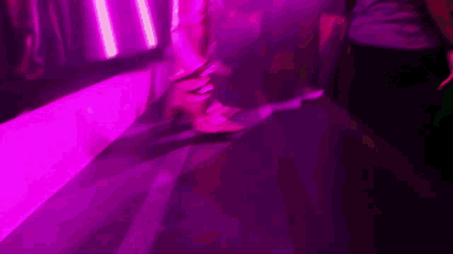 a woman wearing a pair of pink boots is walking in a dark room with purple lights