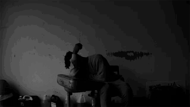 a black and white photo of a person sitting in front of a wall