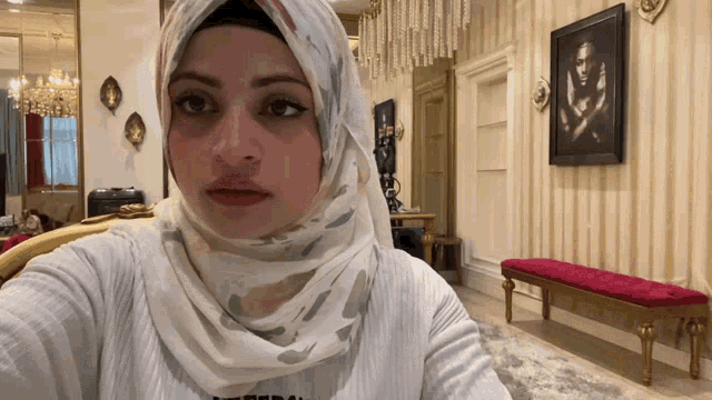 a woman wearing a hijab is taking a selfie in a room