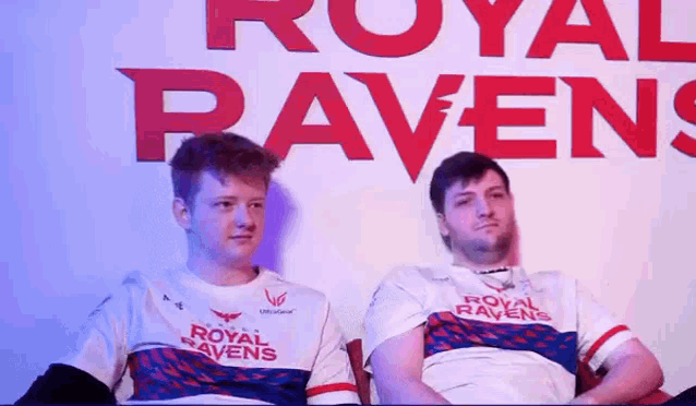 two men are sitting next to each other in front of a sign that says `` royal ravens '' .