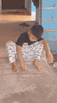 a young boy wearing a black shirt with the letter b on it sits on a concrete surface