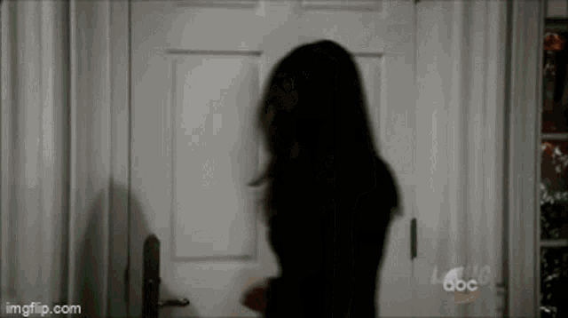 a woman in a black dress is standing in front of a white door with abc written on it