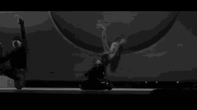 a black and white photo of a woman dancing on a stage with a man behind her .