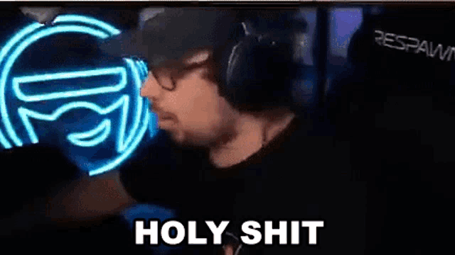 a man wearing headphones and a hat is standing in front of a neon sign and says `` holy shit '' .
