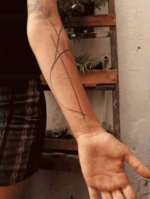 a person with a tattoo on their arm stands in front of a wooden ladder