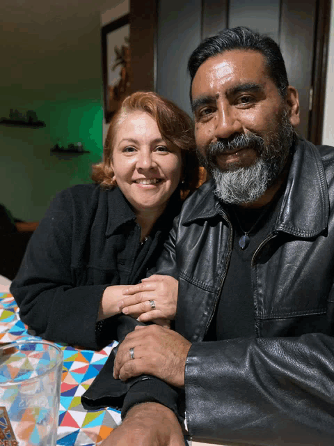 a man and a woman are posing for a picture and the man is wearing a leather jacket