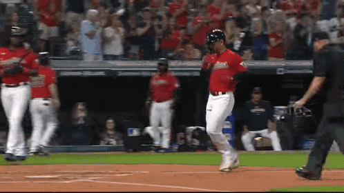 a baseball player is running towards home plate while a referee looks on .