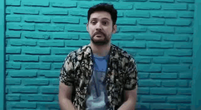 a man with a beard is standing in front of a brick wall and making a funny face .
