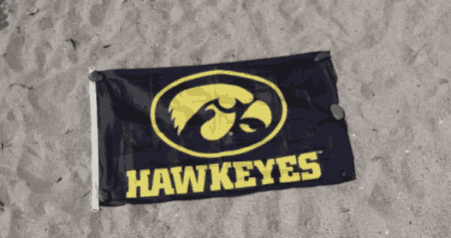 a hawkeyes flag is laying on the sand on the beach