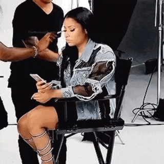 a woman is sitting in a chair holding a cell phone and looking at it .
