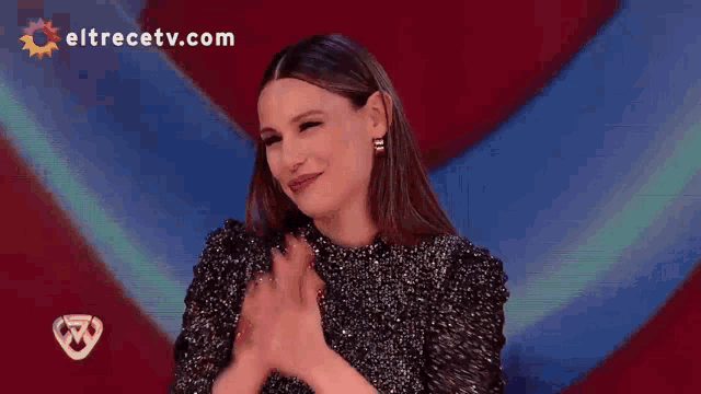a woman is clapping her hands in front of an eltrecetv.com logo