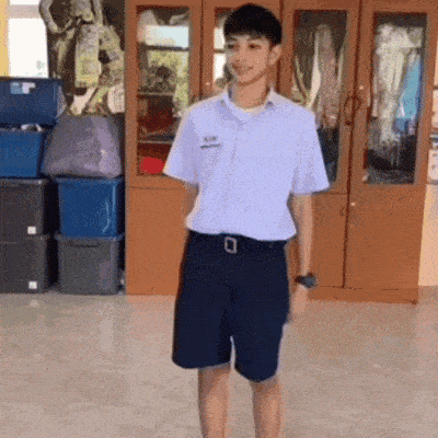 a boy wearing a white shirt and black shorts is standing in front of a cabinet