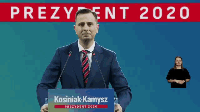 a man in a suit and tie is giving a speech at a podium that says kosinak-kamysz