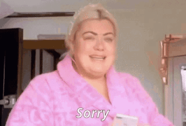 a woman in a pink robe is crying while holding a cell phone and saying sorry .