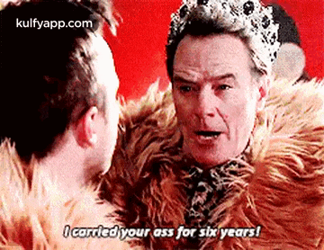 a man wearing a fur coat and a crown is talking to another man wearing a fur coat .