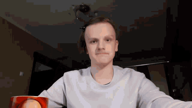 a young man in a white sweater is holding a red cup