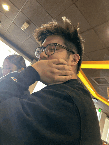 a man wearing glasses and a champion sweatshirt covers his mouth with his hand