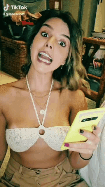 a woman in a white crop top is holding a cell phone and making a funny face with tiktok written on the bottom