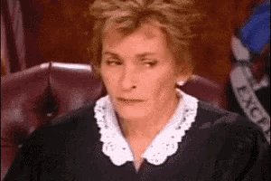 a woman in a judge 's robes is sitting in a chair and looking at the camera
