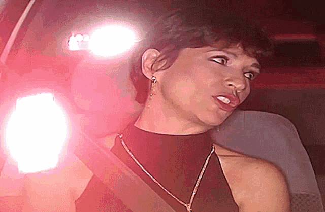 a woman wearing a black top and a gold necklace is sitting in a car