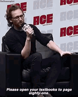a man is sitting in a chair with a microphone in front of a wall that says ace universe