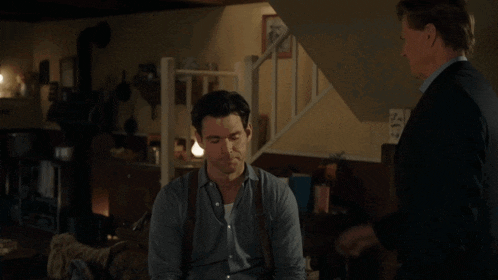 a man in a suit is talking to another man in a room