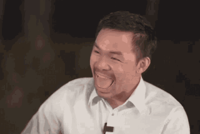 a man in a white shirt is laughing with his eyes closed and his mouth open .