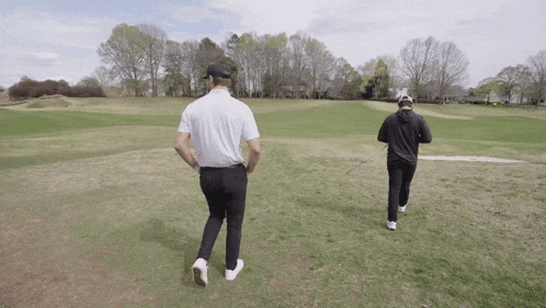 two men are walking on a golf course one is wearing a white shirt