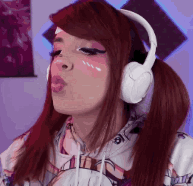 a woman wearing headphones and a hoodie blowing a kiss