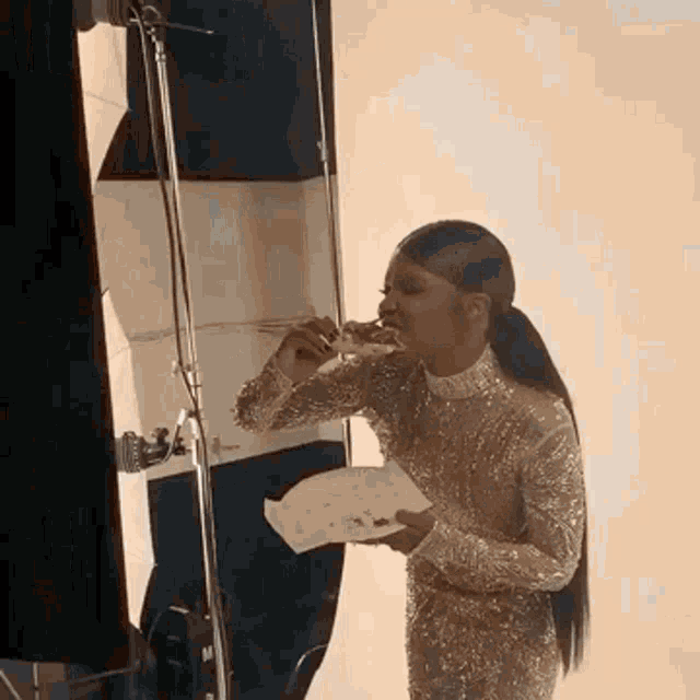 a woman in a gold dress is eating a slice of pizza while holding a plate .