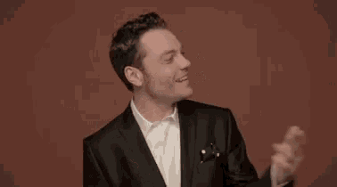 a man in a suit and white shirt is standing in front of a red background .