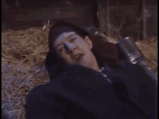 a man wearing a purple hat is laying on a pile of hay
