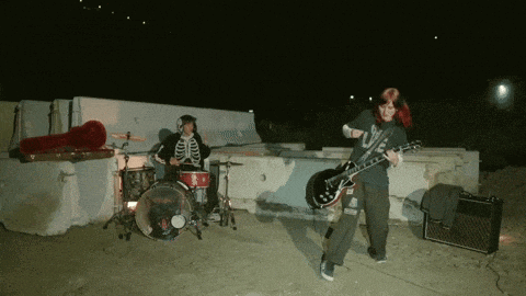a man in a skeleton costume plays drums while a woman plays a guitar