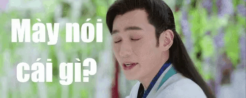 a man with long hair is making a funny face in front of a sign that says may noi cai gi